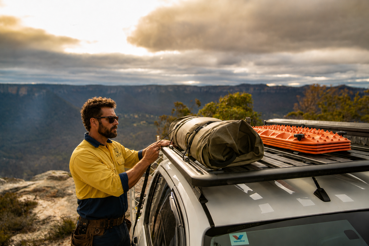 Man securing camping gear on a car roof with a scenic mountain backdrop